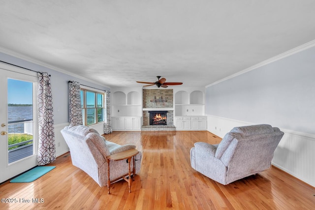 living room featuring ceiling fan, wainscoting, a fireplace, light wood-style floors, and built in features