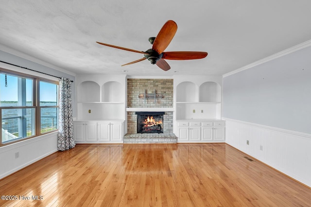 unfurnished living room with a wainscoted wall, ceiling fan, light wood finished floors, and built in shelves