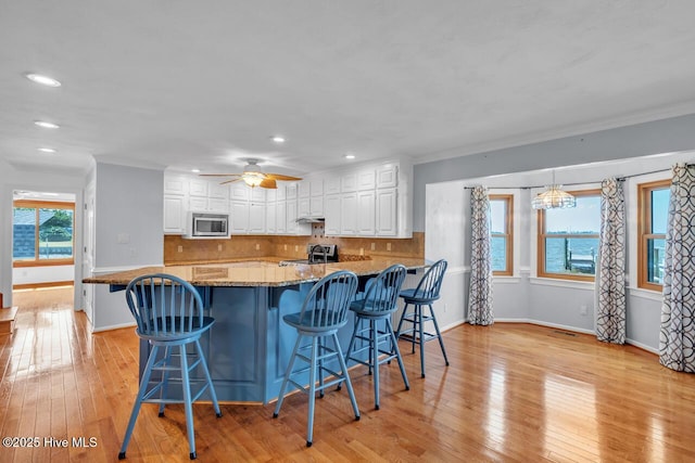 kitchen featuring ornamental molding, dark stone countertops, stainless steel microwave, and white cabinetry