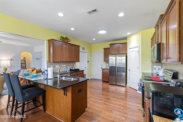 kitchen with stainless steel appliances, a sink, arched walkways, a peninsula, and light wood-style floors