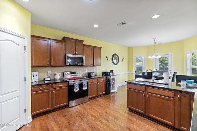 kitchen featuring stainless steel appliances, a sink, light wood-type flooring, backsplash, and a chandelier
