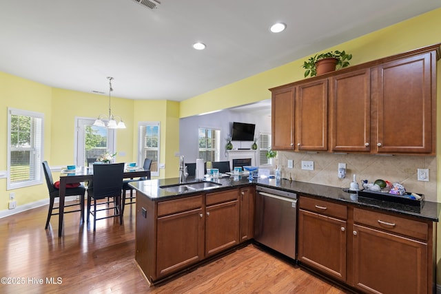 kitchen with dishwasher, a sink, a peninsula, light wood-style flooring, and a chandelier