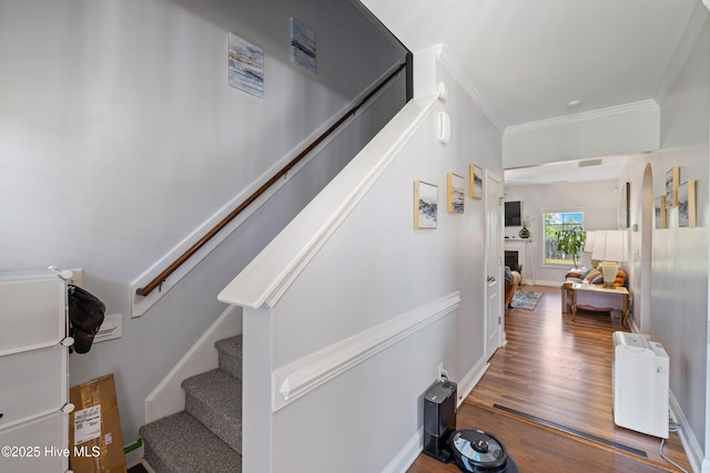stairway featuring crown molding, wood finished floors, baseboards, and a fireplace