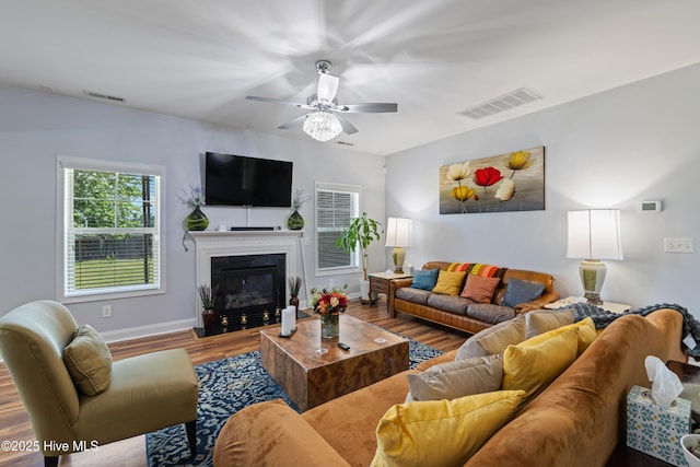 living room featuring wood finished floors, ceiling fan, baseboards, and a glass covered fireplace