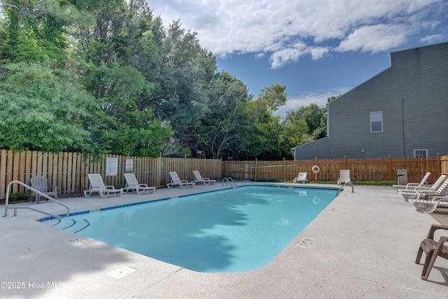 community pool featuring a patio, fence, and view of wooded area