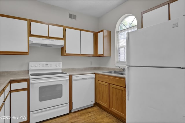 kitchen featuring white appliances, under cabinet range hood, a sink, light wood-type flooring, and light countertops