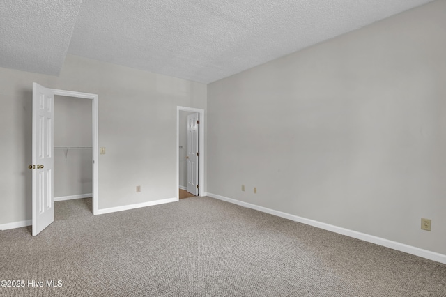 unfurnished bedroom with carpet flooring, a textured ceiling, baseboards, and a spacious closet