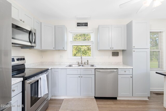 kitchen featuring appliances with stainless steel finishes, a sink, light countertops, light wood-style flooring, and a ceiling fan