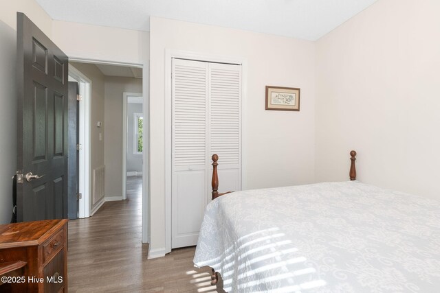 bedroom featuring baseboards, a closet, wood finished floors, and visible vents