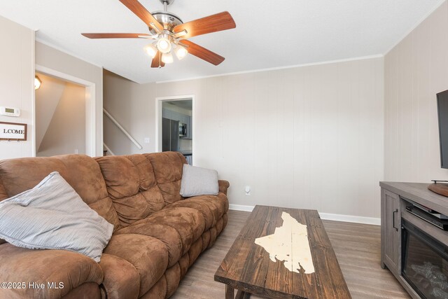 living room featuring a ceiling fan, crown molding, wood finished floors, stairway, and baseboards