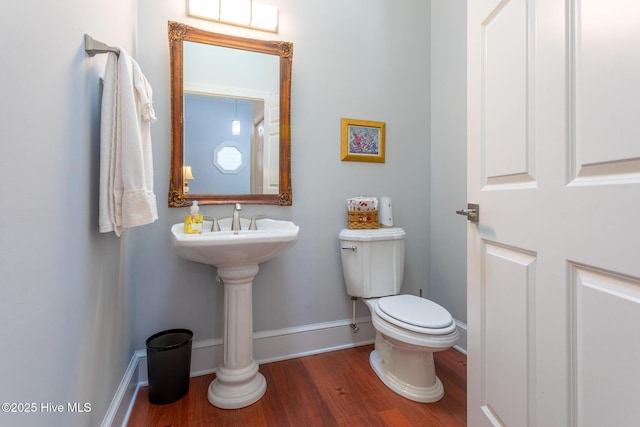 half bath with toilet, baseboards, and wood finished floors