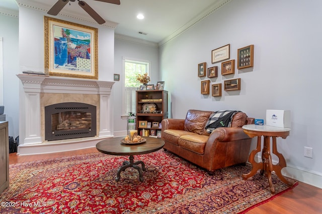 living room featuring a ceiling fan, visible vents, crown molding, a tiled fireplace, and wood finished floors
