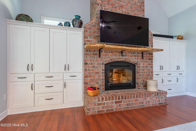 living area featuring baseboards, a brick fireplace, wood finished floors, and lofted ceiling