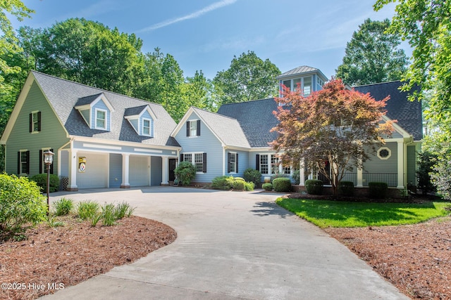 cape cod-style house featuring an attached garage, a shingled roof, driveway, and covered porch