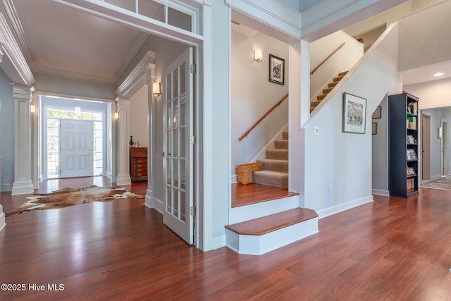 staircase with baseboards, decorative columns, ornamental molding, and wood finished floors