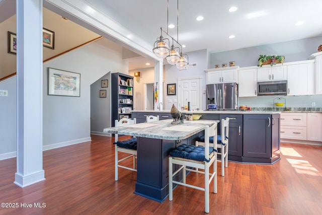 kitchen with a kitchen bar, a center island, white cabinets, stainless steel appliances, and dark wood-type flooring