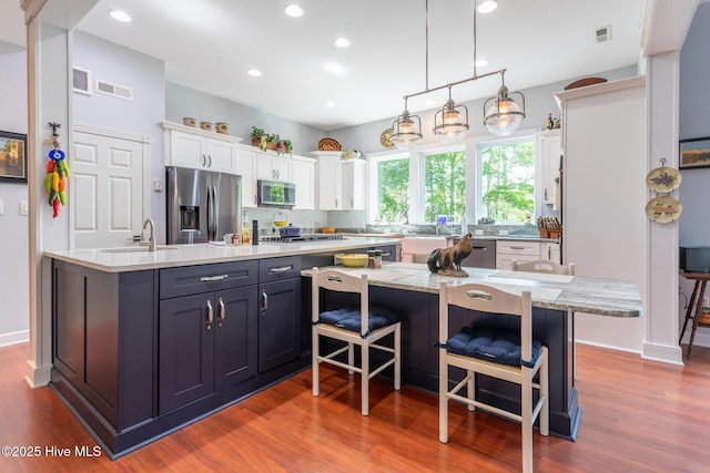 kitchen with visible vents, a center island with sink, light countertops, white cabinets, and stainless steel appliances