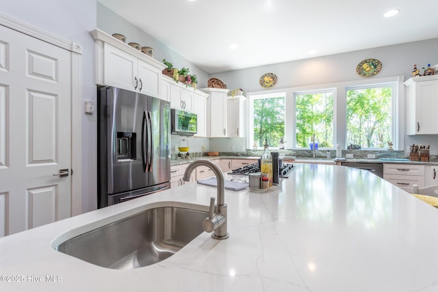 kitchen with white cabinets, light stone countertops, appliances with stainless steel finishes, a sink, and recessed lighting