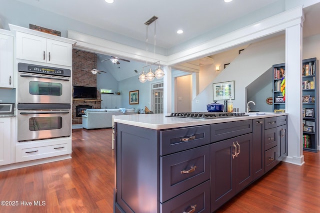 kitchen with ceiling fan, appliances with stainless steel finishes, vaulted ceiling, white cabinets, and open floor plan