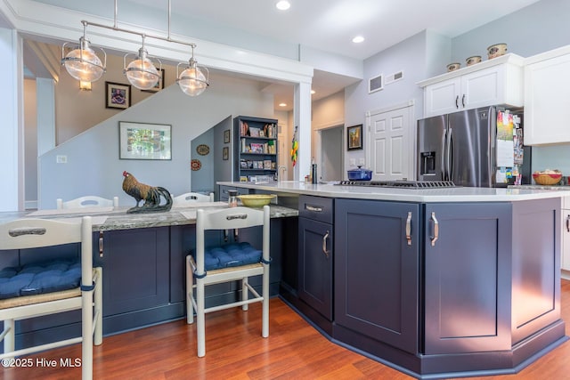 kitchen featuring white cabinets, a breakfast bar, stainless steel appliances, wood finished floors, and visible vents