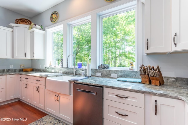 kitchen with stainless steel dishwasher, dark wood finished floors, a sink, light stone counters, and white cabinets
