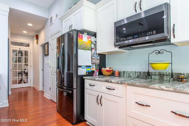 kitchen featuring white cabinets, light stone countertops, appliances with stainless steel finishes, and dark wood-type flooring
