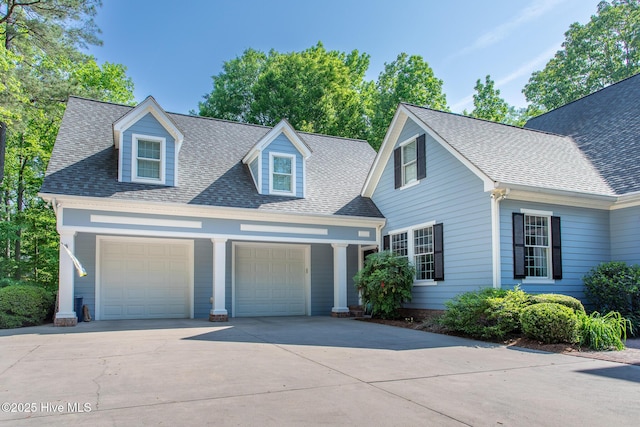 cape cod house with an attached garage, roof with shingles, and concrete driveway