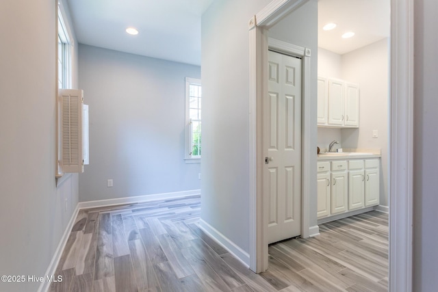 hallway featuring light wood-style floors, baseboards, recessed lighting, and a sink