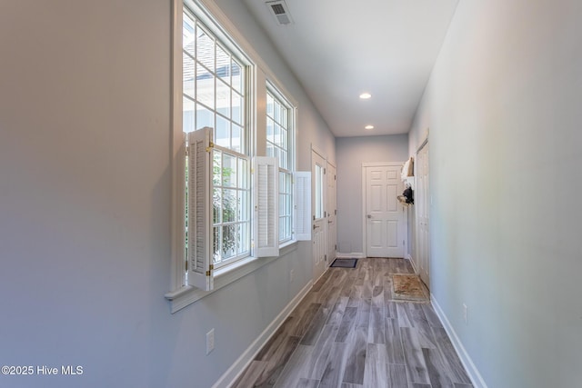 corridor with baseboards, visible vents, plenty of natural light, and wood finished floors