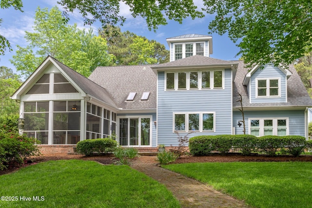 rear view of house with a sunroom, a lawn, and roof with shingles