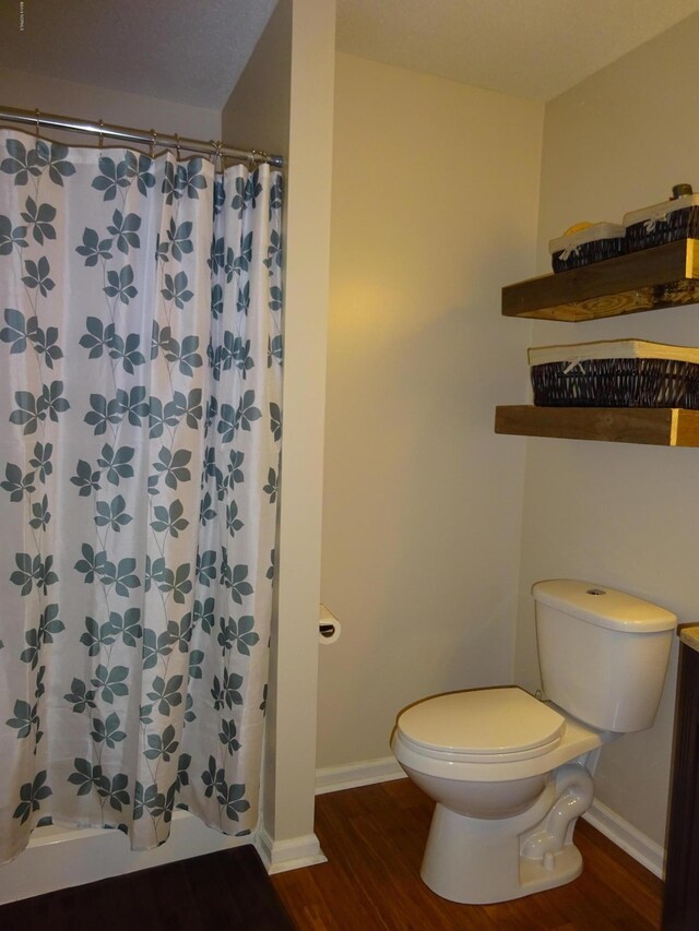 bathroom with baseboards, a shower with curtain, toilet, and wood finished floors