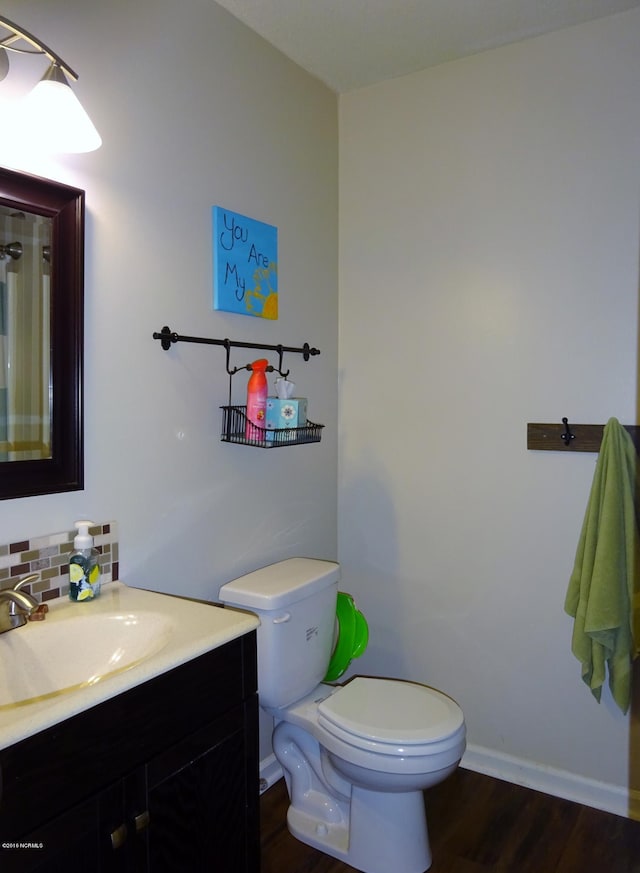 bathroom with vanity, wood finished floors, toilet, baseboards, and tasteful backsplash