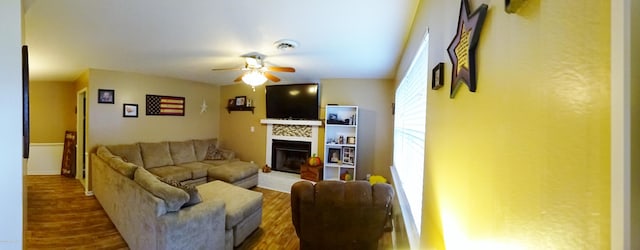 living area featuring a ceiling fan, a fireplace with raised hearth, and wood finished floors
