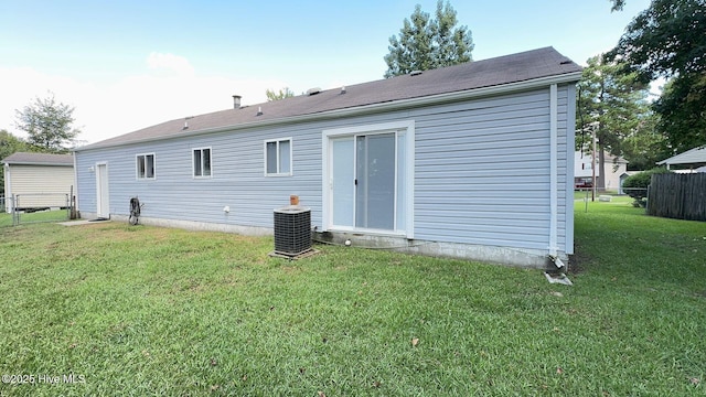 rear view of property featuring central air condition unit, fence, and a yard