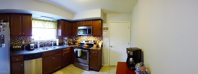 kitchen with dark countertops, tasteful backsplash, a sink, stainless steel appliances, and reddish brown cabinets