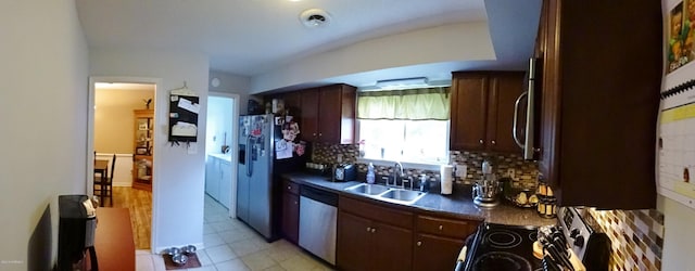 kitchen with decorative backsplash, dark brown cabinetry, dark countertops, a sink, and stainless steel appliances