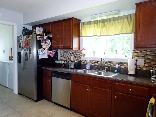 kitchen featuring light tile patterned flooring, dark countertops, separate washer and dryer, a sink, and appliances with stainless steel finishes