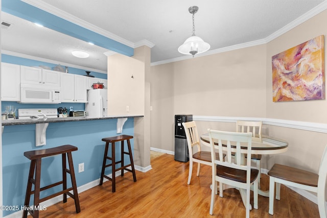 dining area with light wood-style floors, baseboards, and crown molding
