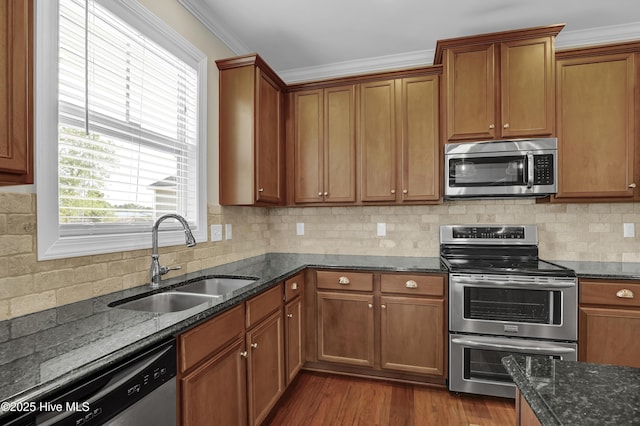 kitchen featuring crown molding, a sink, dark stone counters, and stainless steel appliances