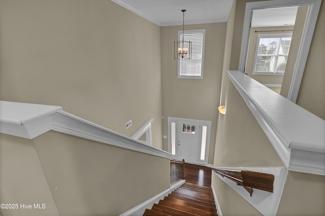 stairs with baseboards, an inviting chandelier, ornamental molding, and wood finished floors