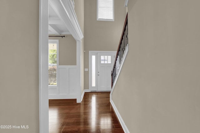 entrance foyer with dark wood-style flooring, wainscoting, a decorative wall, beamed ceiling, and stairway
