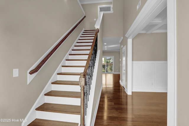 stairs featuring crown molding, a high ceiling, wood finished floors, and a decorative wall
