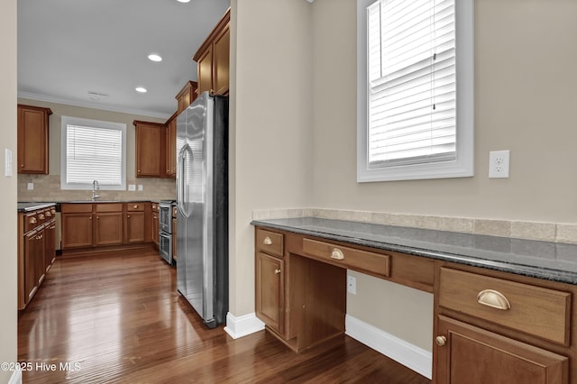 kitchen featuring dark wood-style flooring, a sink, brown cabinetry, stainless steel appliances, and decorative backsplash