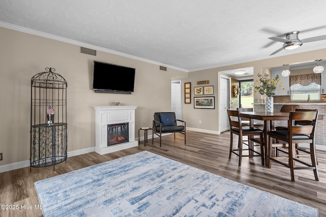 interior space featuring ceiling fan, visible vents, wood finished floors, baseboards, and a glass covered fireplace