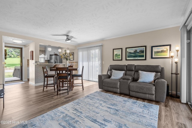 living area with a textured ceiling, ceiling fan, ornamental molding, and wood finished floors