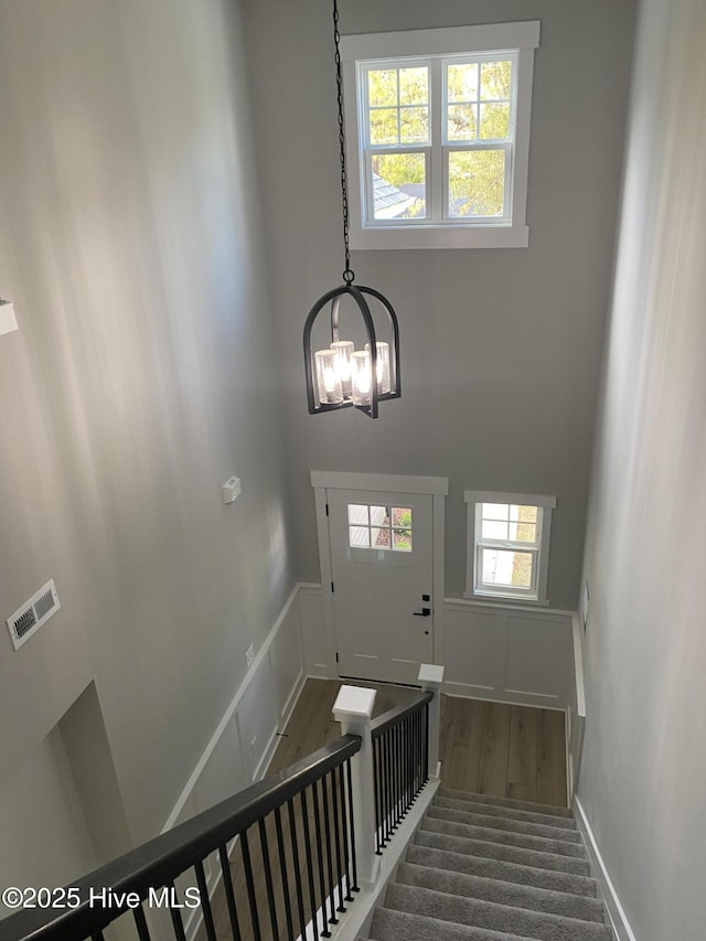 staircase featuring visible vents, an inviting chandelier, a decorative wall, wood finished floors, and a wainscoted wall