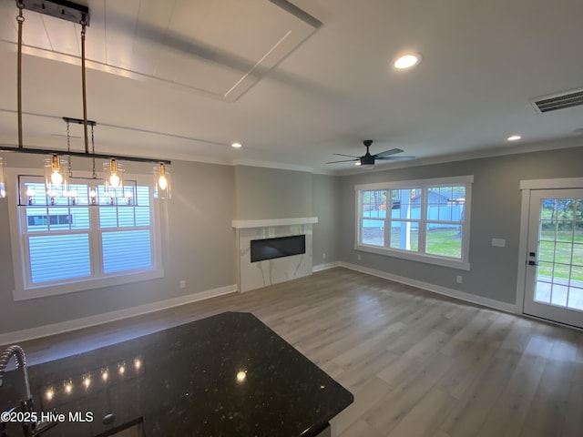unfurnished living room featuring visible vents, a glass covered fireplace, wood finished floors, baseboards, and recessed lighting