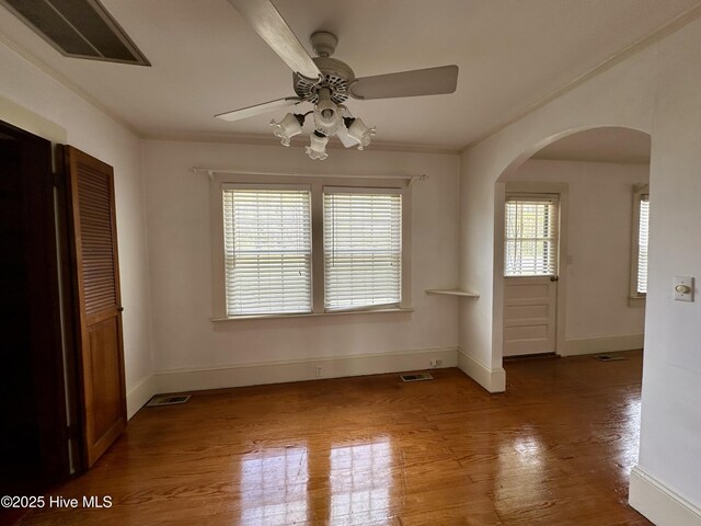 spare room with arched walkways, ceiling fan, wood finished floors, and visible vents
