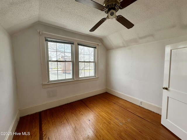additional living space featuring a textured ceiling, vaulted ceiling, baseboards, and hardwood / wood-style floors