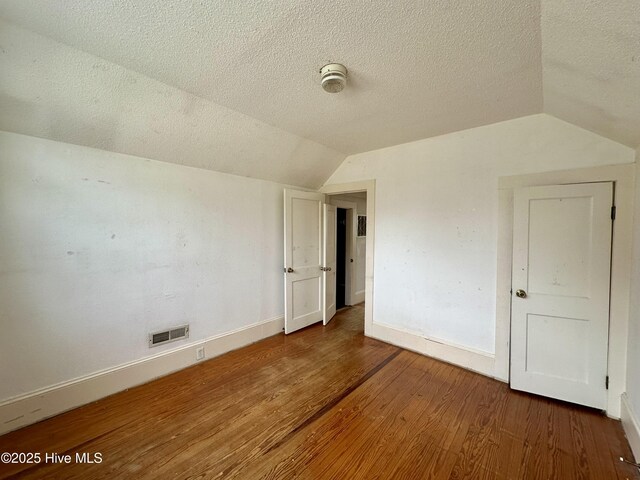 additional living space featuring a textured ceiling, baseboards, wood finished floors, lofted ceiling, and visible vents